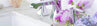 Close-up of a modern polished chrome bathroom faucet on a white marble vanity, decorated with purple flowers.